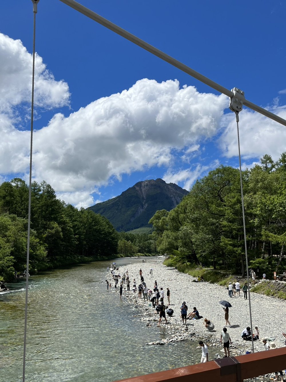 The clear Azusa River in Kamikochi leading to Yakedake volcano under a blue summer sky with visitors on the riverbank