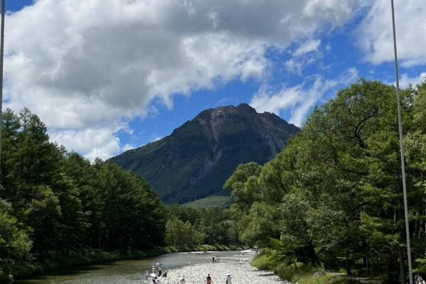 The clear Azusa River in Kamikochi leading to Yakedake volcano under a blue summer sky with visitors on the riverbank