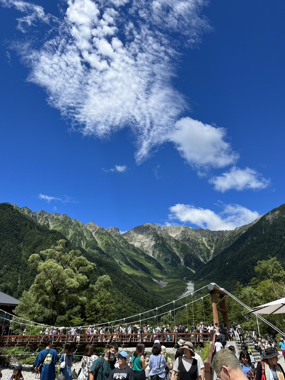 Kappa Bridge in Kamikochi crowded with visitors below the jagged Hotaka mountain range on a clear day