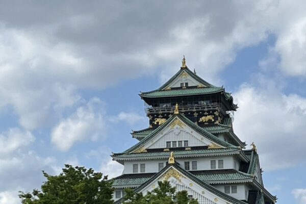 Osaka Castle main keep with green roofs and gold trim rising above the park on a partly cloudy day
