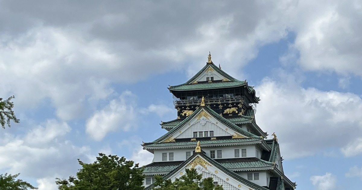 Osaka Castle main keep with green roofs and gold trim rising above the park on a partly cloudy day