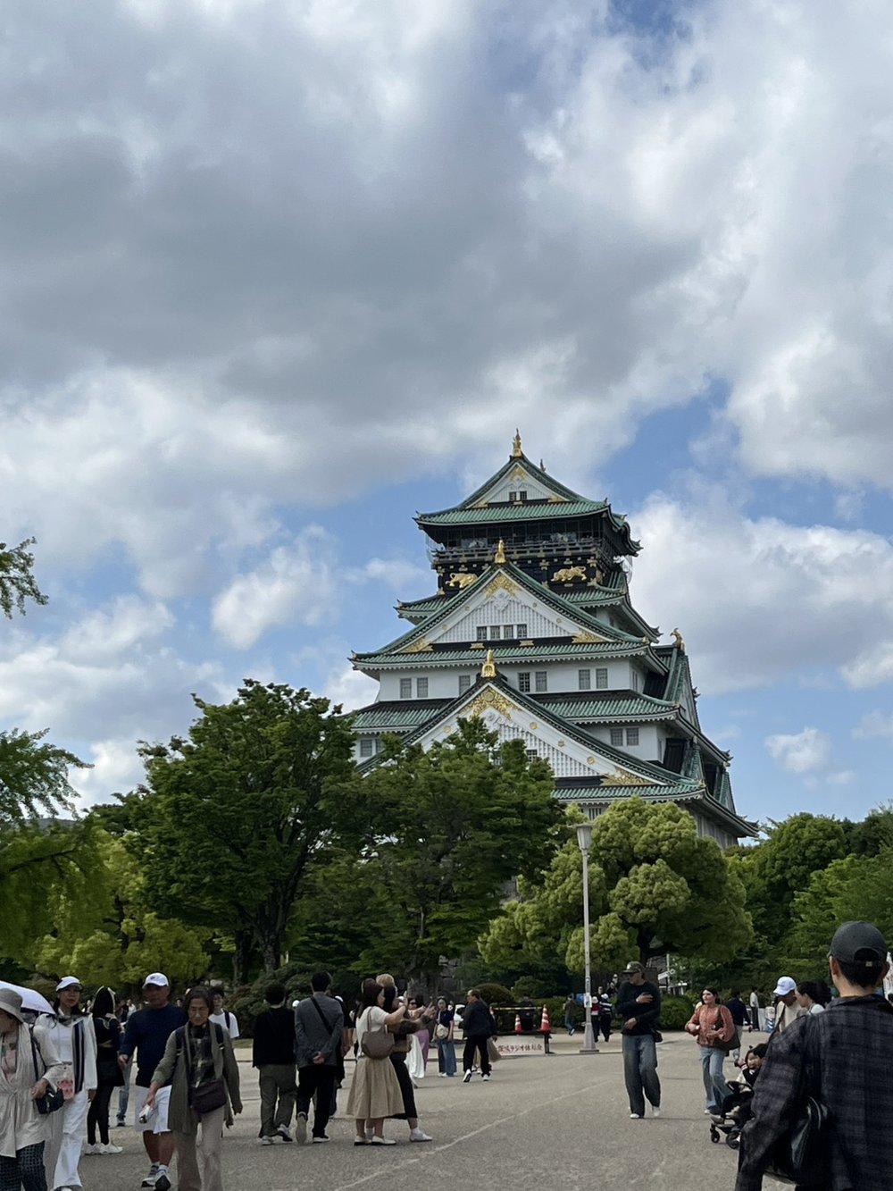 Osaka Castle main keep with green roofs and gold trim rising above the park on a partly cloudy day